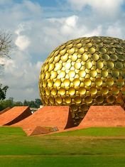 The golden Matrimandir dome surrounded by lawns and trees in Auroville
