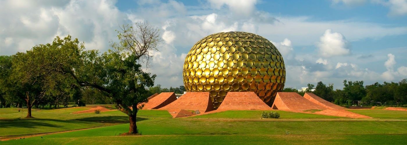 The golden Matrimandir dome surrounded by lawns and trees in Auroville