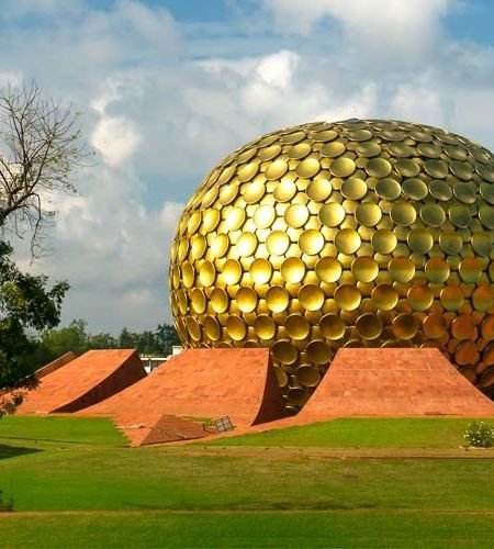 The golden Matrimandir dome surrounded by lawns and trees in Auroville